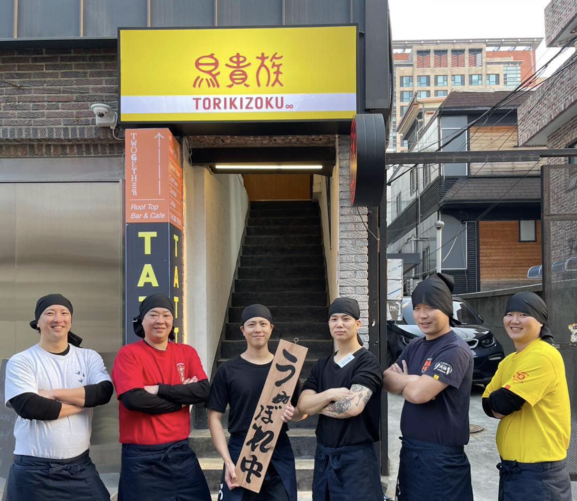 鳥貴族の店舗前で腕を組んで並ぶ6人のスタッフ